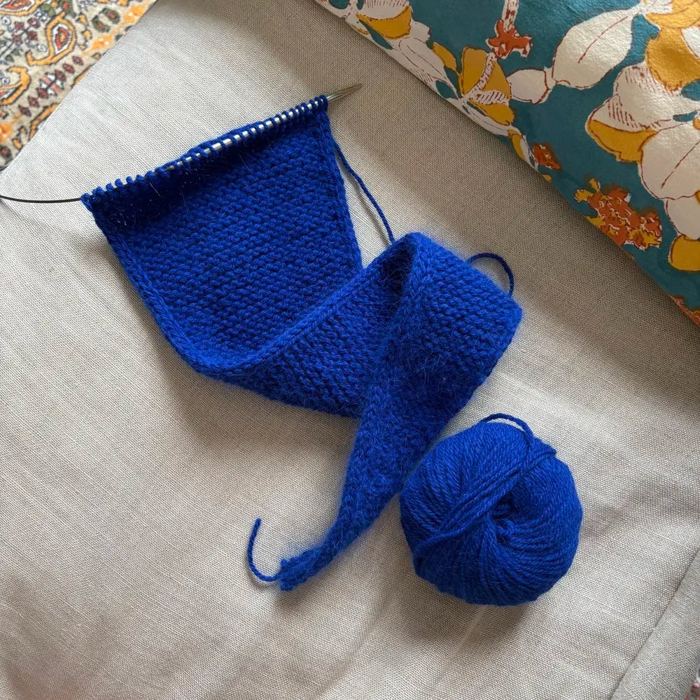 tricot en cours de couleur bleu klein posé sur un canapé en lin beige