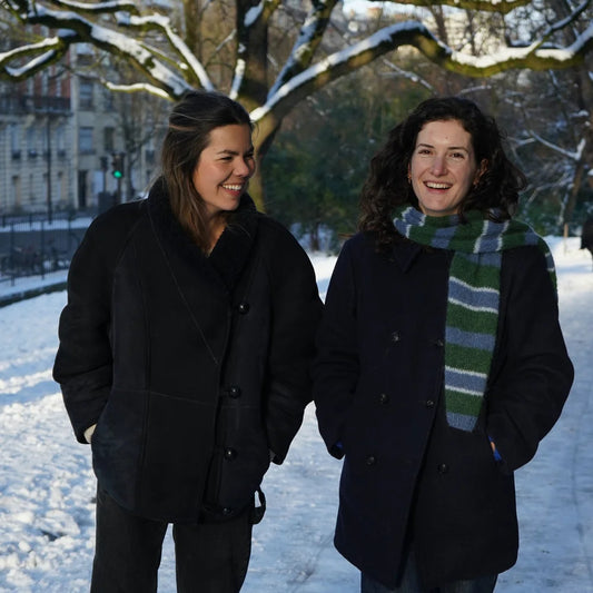 2 femmes marchant dans la neige, celle de gauche sourit et regarde vers la droite, celle de droite porte une écharpe rayée bleu et verte