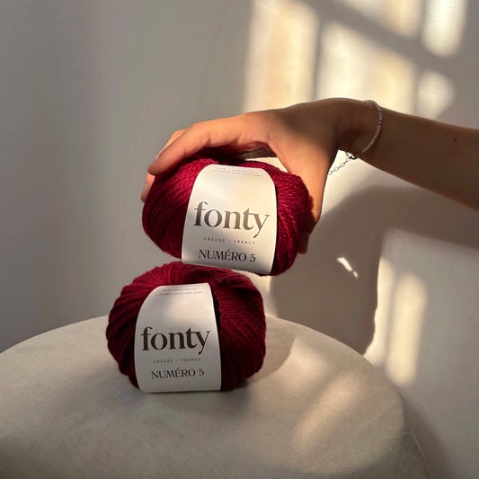 2 pelotes de laine numéro 5 bordeaux posées par une main