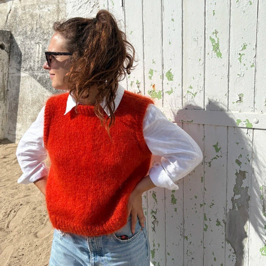 femme portant un pull sans manches orange en mohair tricoté à la main sur une plage
