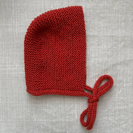 béguin de naissance orange brulé par tricotant posé sur du lin beige