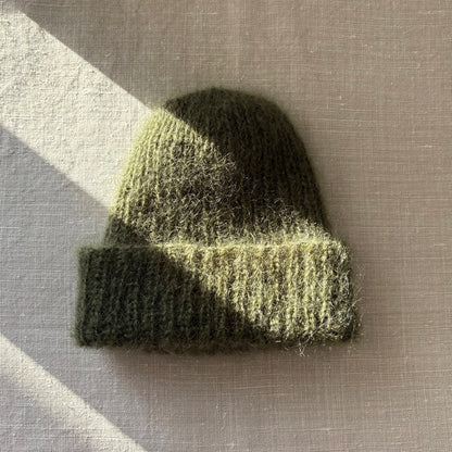 bonnet en mohair vert kaki posé sur du lin avec un rayon de soleil