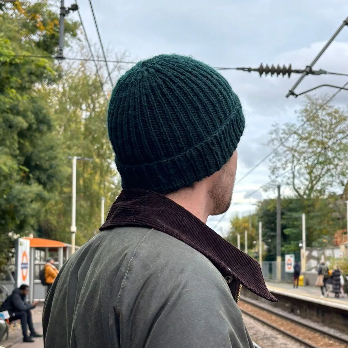 homme de dos sur un quai de gare portant un bonnet vert