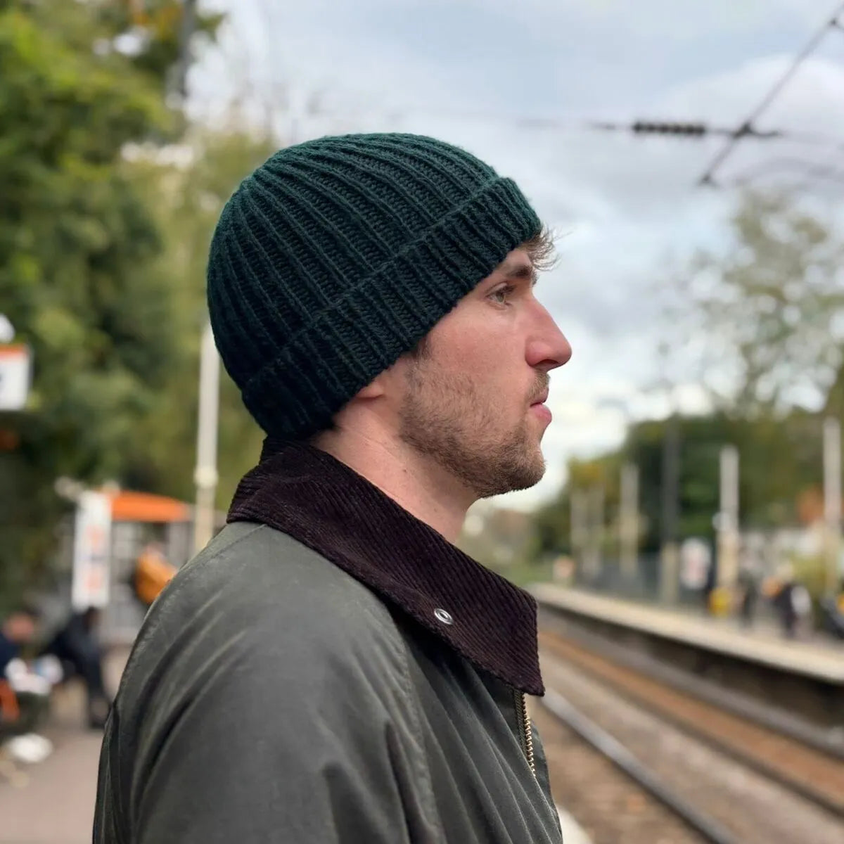 homme de profil sur un quai de gare portant un bonnet en laine vert