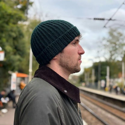 homme de profil sur un quai de gare portant un bonnet en laine vert