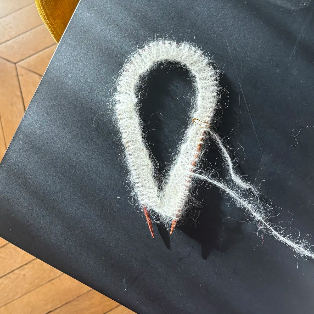 tricot en cours d'un bonnet en mohair écru posé sur une table noire