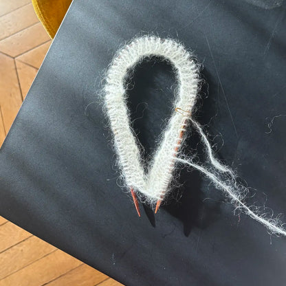 tricot en cours d'un bonnet en mohair écru posé sur une table noire