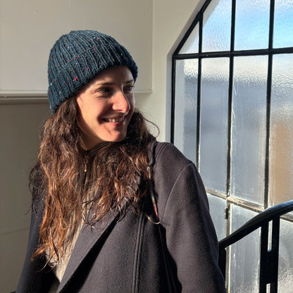 femme aux cheveux longs dans un hall d'escalier souriant et portant un bonnet en tweed bleu marine