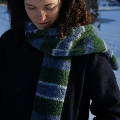 femme brune regardant son écharpe rayée vert et bleu tricotée