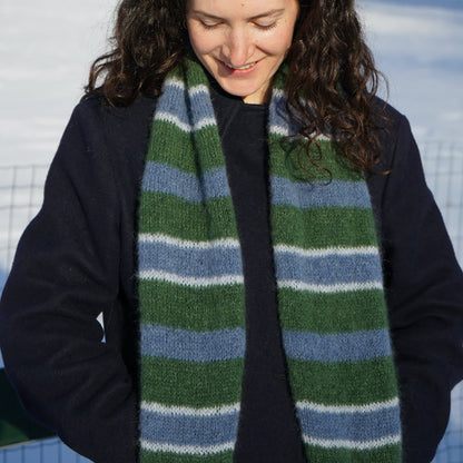 femme brune baissant la tête et souriant, regardant une écharpe rayée bleu et verte tricotée