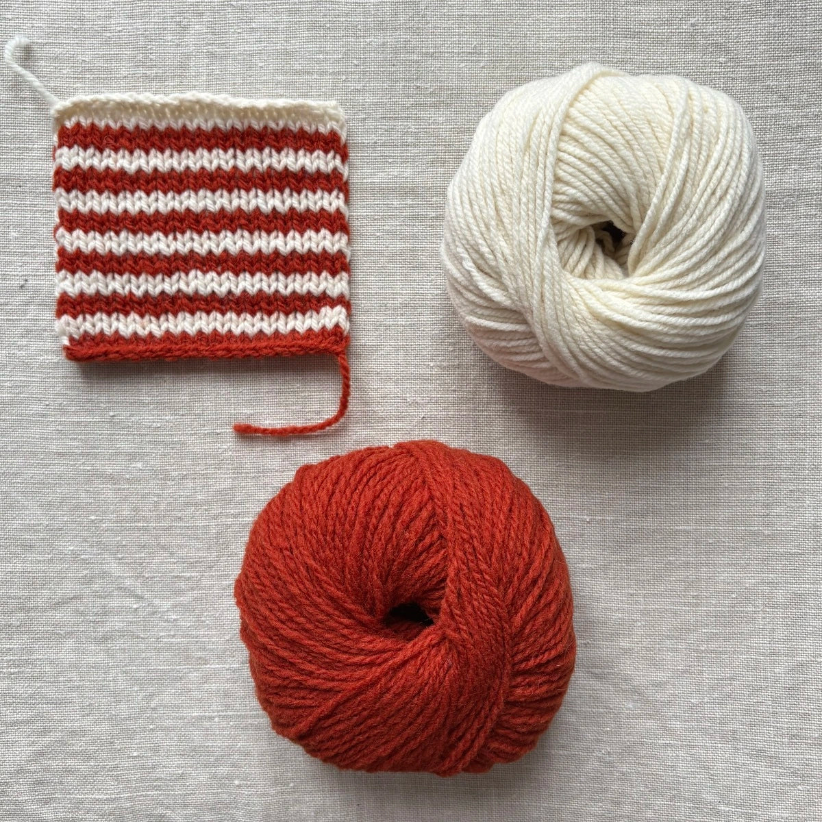 échantillon de laine tricotée avec des rayures écrues et rouille et pelotes correspondantes à côté