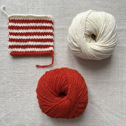 échantillon de laine tricotée avec des rayures écrues et rouille et pelotes correspondantes à côté