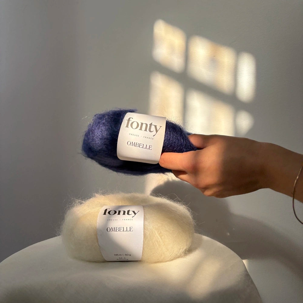 pelotes de mohair bleu marine et écrue posées par une main l'une sur l'autre