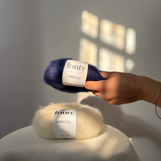 pelotes de mohair bleu marine et écrue posées par une main l'une sur l'autre