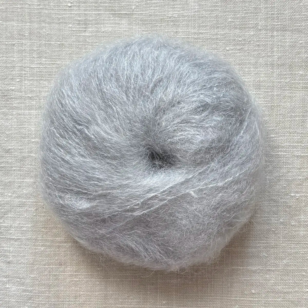pelote de laine mohair à tricoter de la marque fonty, de couleur gris perle sur fond de lin beige