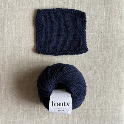 Pelote de laine ethique 1880 coloris bleu marine de Fonty – boutique Tricotant, vue de dessus sur fond lin avec échantillon tricoté