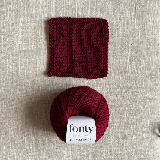 Pelote de laine BB Mérinos coloris bordeaux de Fonty – boutique Tricotant, vue de dessus sur fond lin avec échantillon tricoté