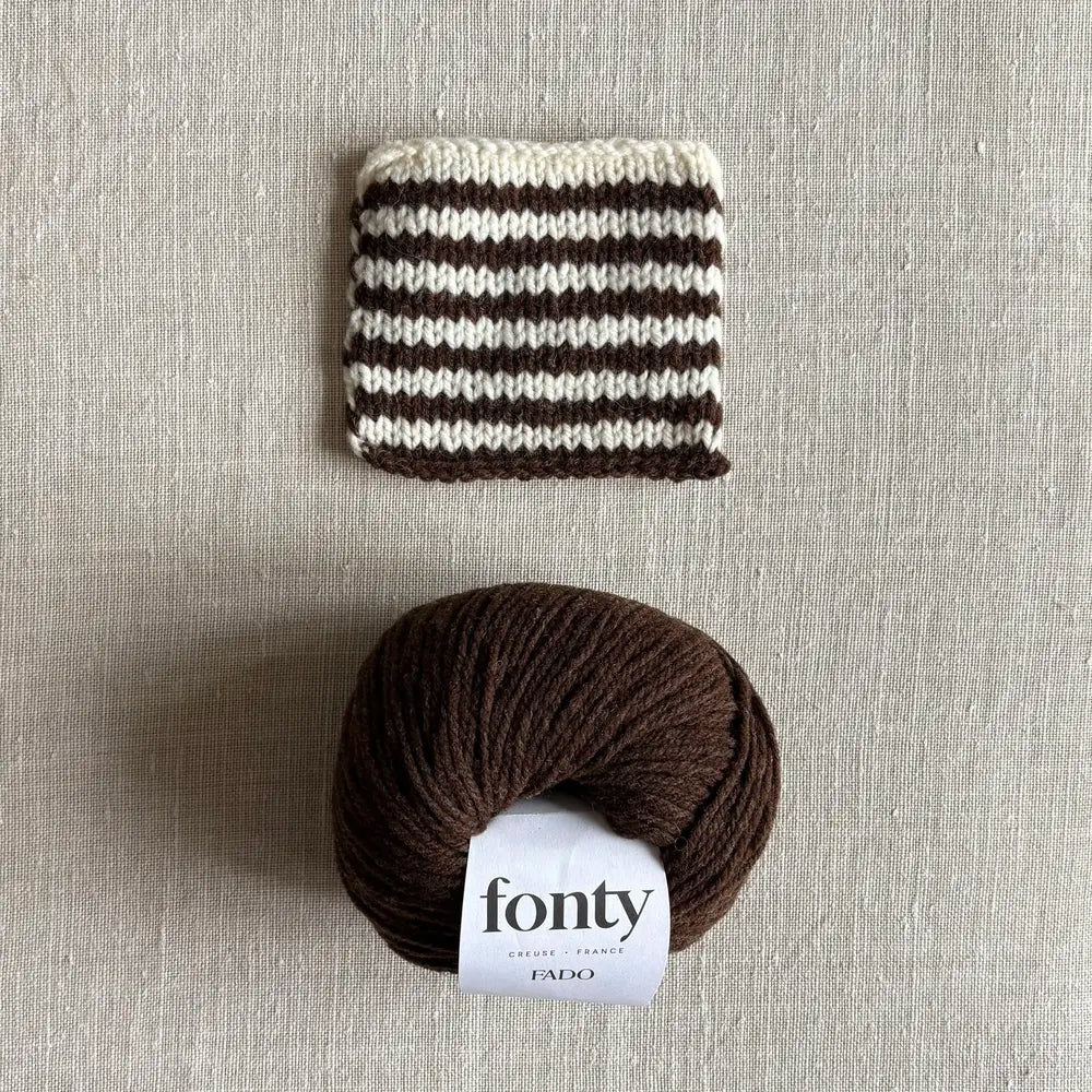 Pelote de laine Fado coloris marron de Fonty – boutique Tricotant, vue de dessus sur fond lin avec échantillon rayé écru marron tricoté