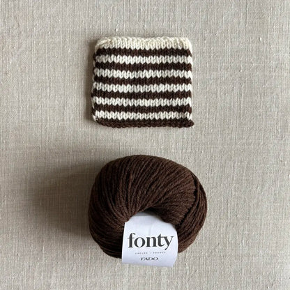 Pelote de laine Fado coloris marron de Fonty – boutique Tricotant, vue de dessus sur fond lin avec échantillon rayé écru marron tricoté