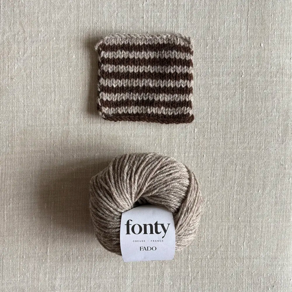 Pelote de laine Fado coloris beige chiné de Fonty – boutique Tricotant, vue de dessus sur fond lin avec échantillon rayé beige chiné marron tricoté