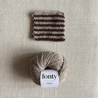 Pelote de laine Fado coloris beige chiné de Fonty – boutique Tricotant, vue de dessus sur fond lin avec échantillon rayé beige chiné marron tricoté