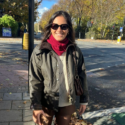 femme qui marche dans la rue et porte un bandana tricoté à la main bordeaux, avec une veste barbour et des lunettes de soleil